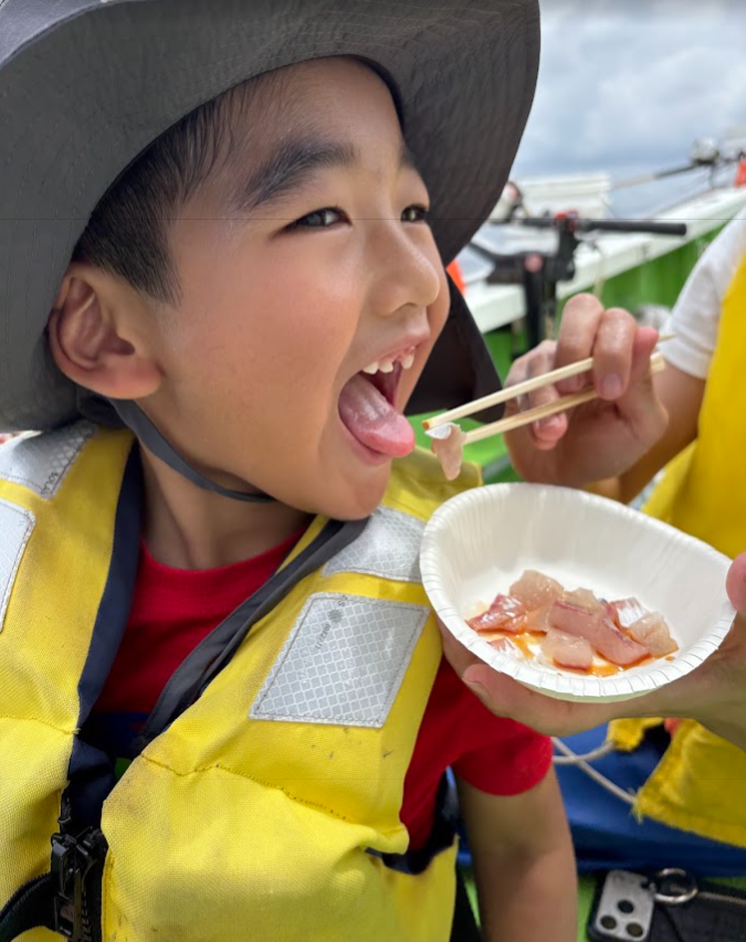 船の上で、釣れたてのお刺身を食べる子ども
